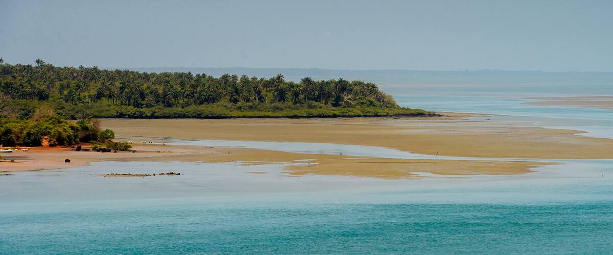A coastal landscape with a sandy beach, turquoise waters, and a forested peninsula.