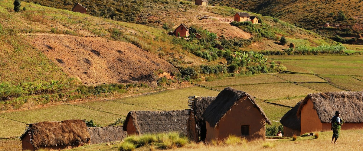 A rural landscape with terraced fields, thatched-roof houses, and rolling hills.