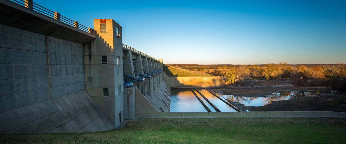 A concrete dam with a spillway, a bridge, and a calm river below.