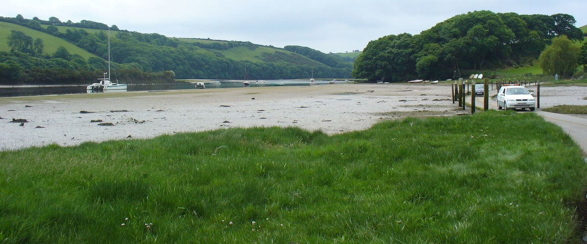 A coastal landscape with a sandy beach, boats, and a car parked near a fence.