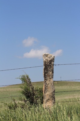 Stone post fence with green grass and blue sky with clouds north of Lucas Kansas USA out in the country.