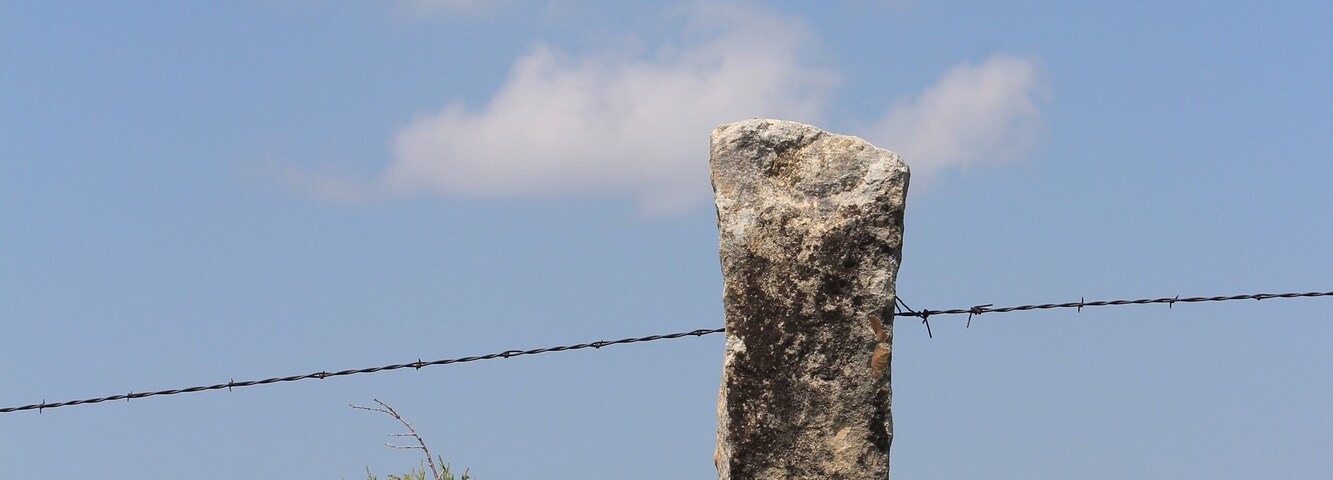 Stone post fence with green grass and blue sky with clouds north of Lucas Kansas USA out in the country.