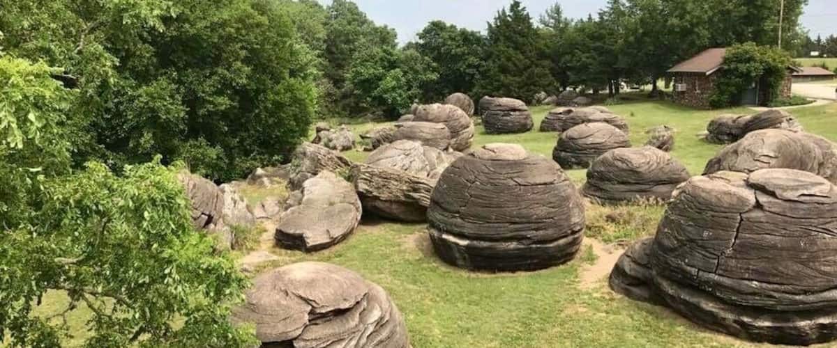 A landscape with large, rounded boulders and a grassy area with trees and a small building in the background.