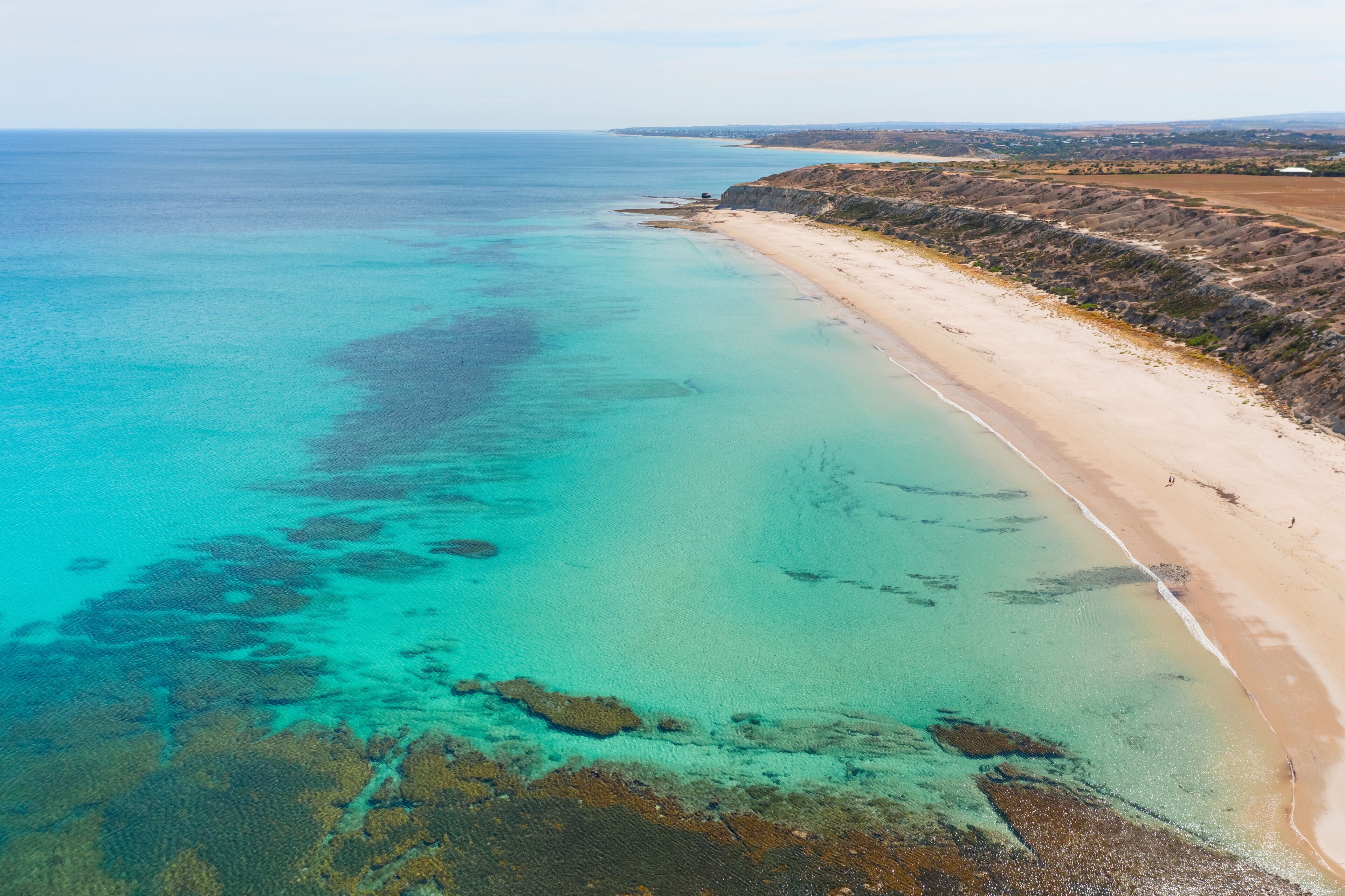 Un paisaje costero con una playa arenosa, aguas turquesas cristalinas y acantilados rocosos.