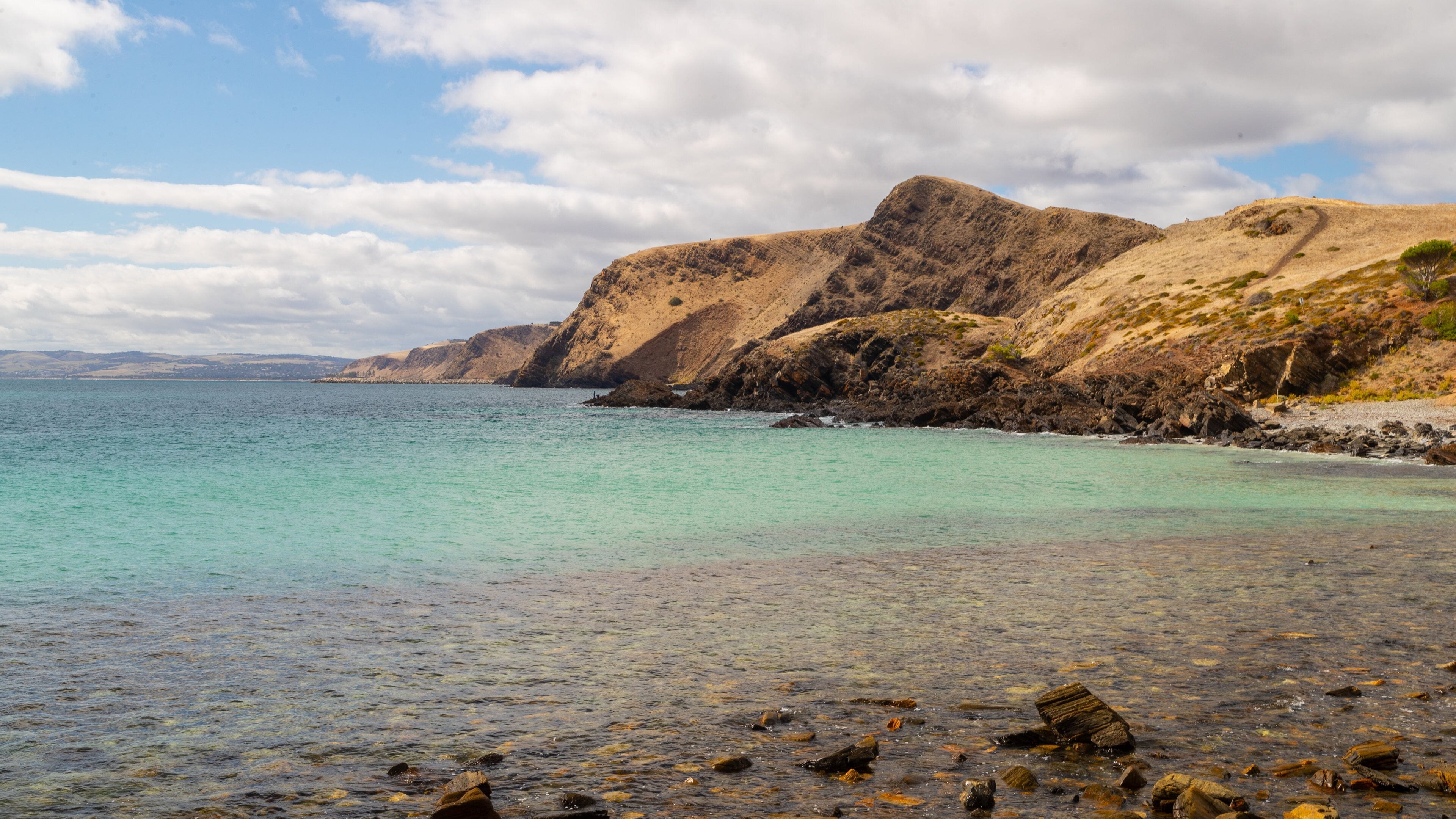 A coastal landscape with clear turquoise waters, rocky cliffs, and a sandy beach.