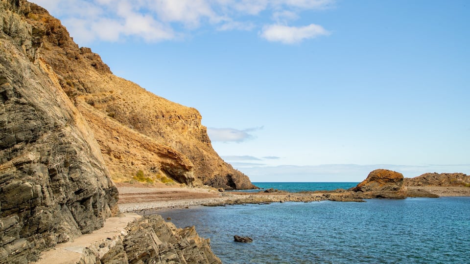 A coastal landscape with rocky cliffs, a clear blue sea, and a narrow path leading to the beach.