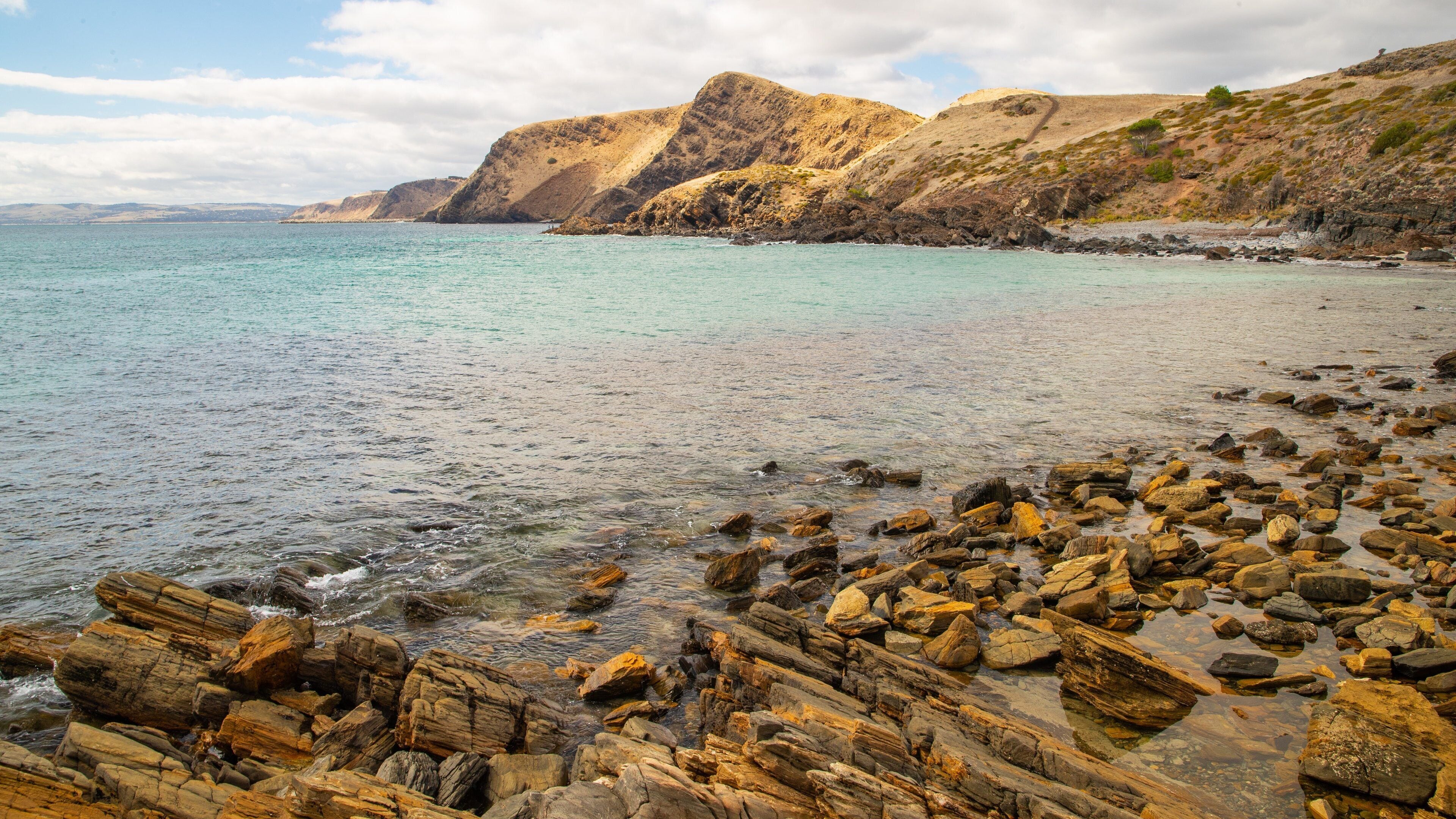 A rocky beach with clear turquoise water and distant hills.