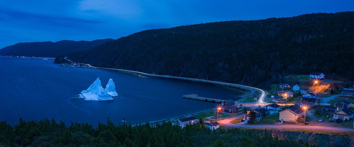 A coastal town at dusk with a lighthouse, icebergs, and a bridge.