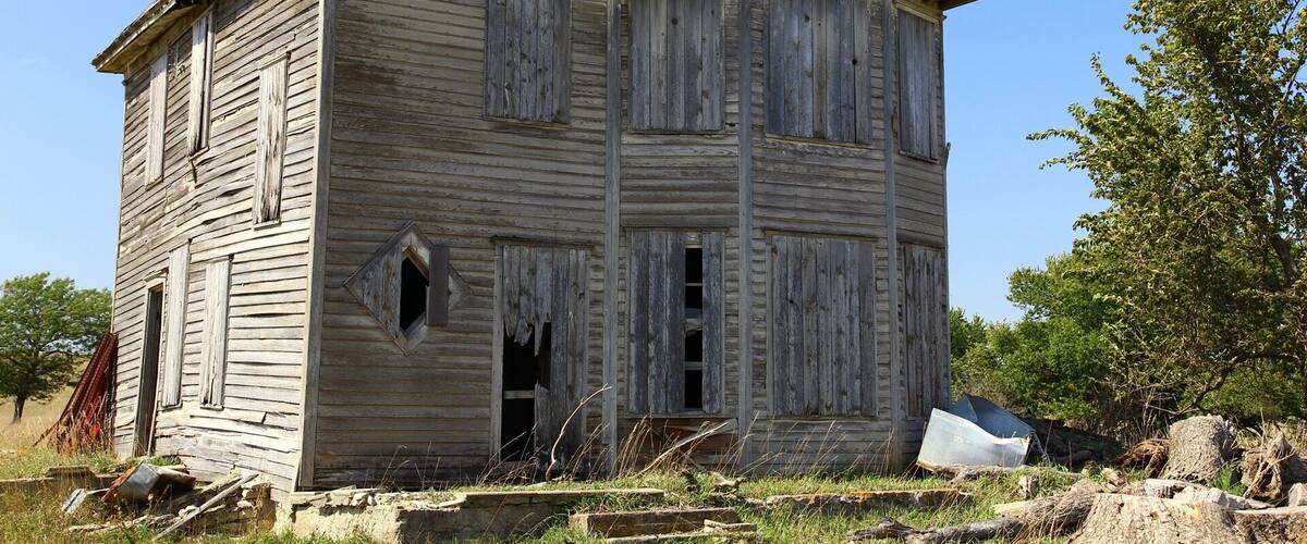 An old wooden house with boarded-up windows and a dilapidated roof.