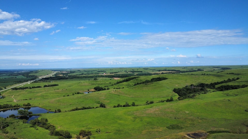 A vast green landscape with rolling hills, a small body of water, and a distant road.
