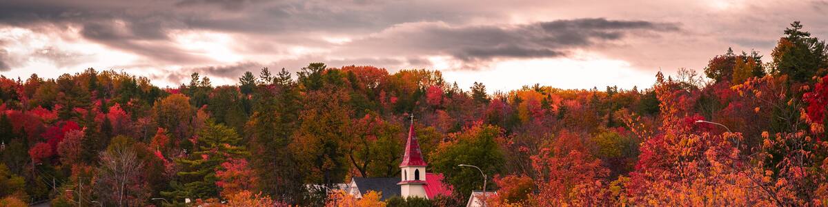Autumn in picturesque village of Wakefield, boats on the Gatineau River, red church steeple, colourful foliage fall season, dramatic sky cloudscape, La Peche, Outaouais, Quebec, Canada, October 2022