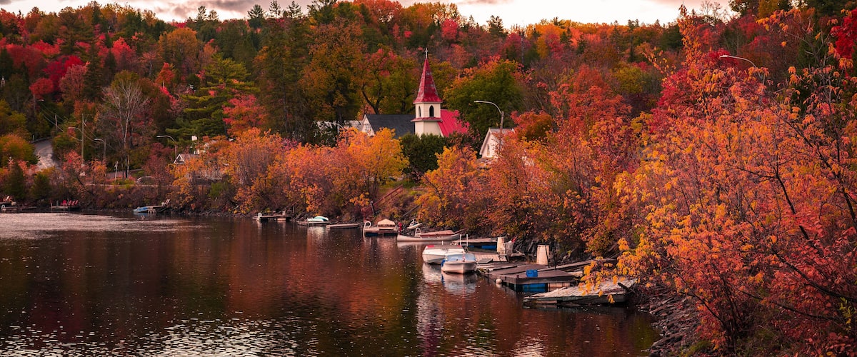 Autumn in picturesque village of Wakefield, boats on the Gatineau River, red church steeple, colourful foliage fall season, dramatic sky cloudscape, La Peche, Outaouais, Quebec, Canada, October 2022
