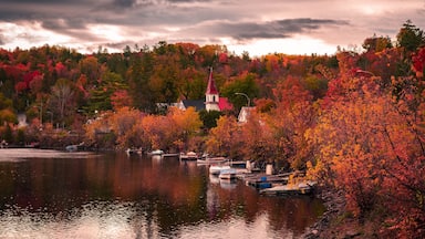 Autumn in picturesque village of Wakefield, boats on the Gatineau River, red church steeple, colourful foliage fall season, dramatic sky cloudscape, La Peche, Outaouais, Quebec, Canada, October 2022