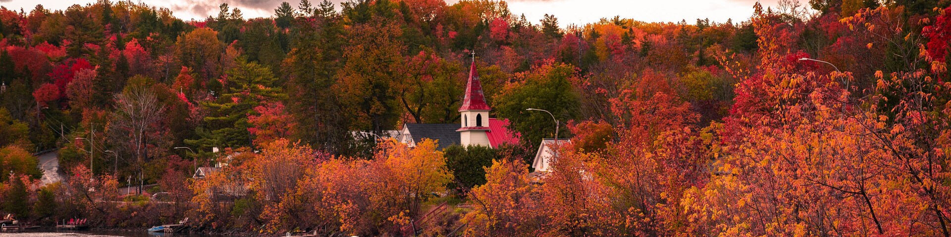 A lake with boats, autumn trees, and a church on a hill.
