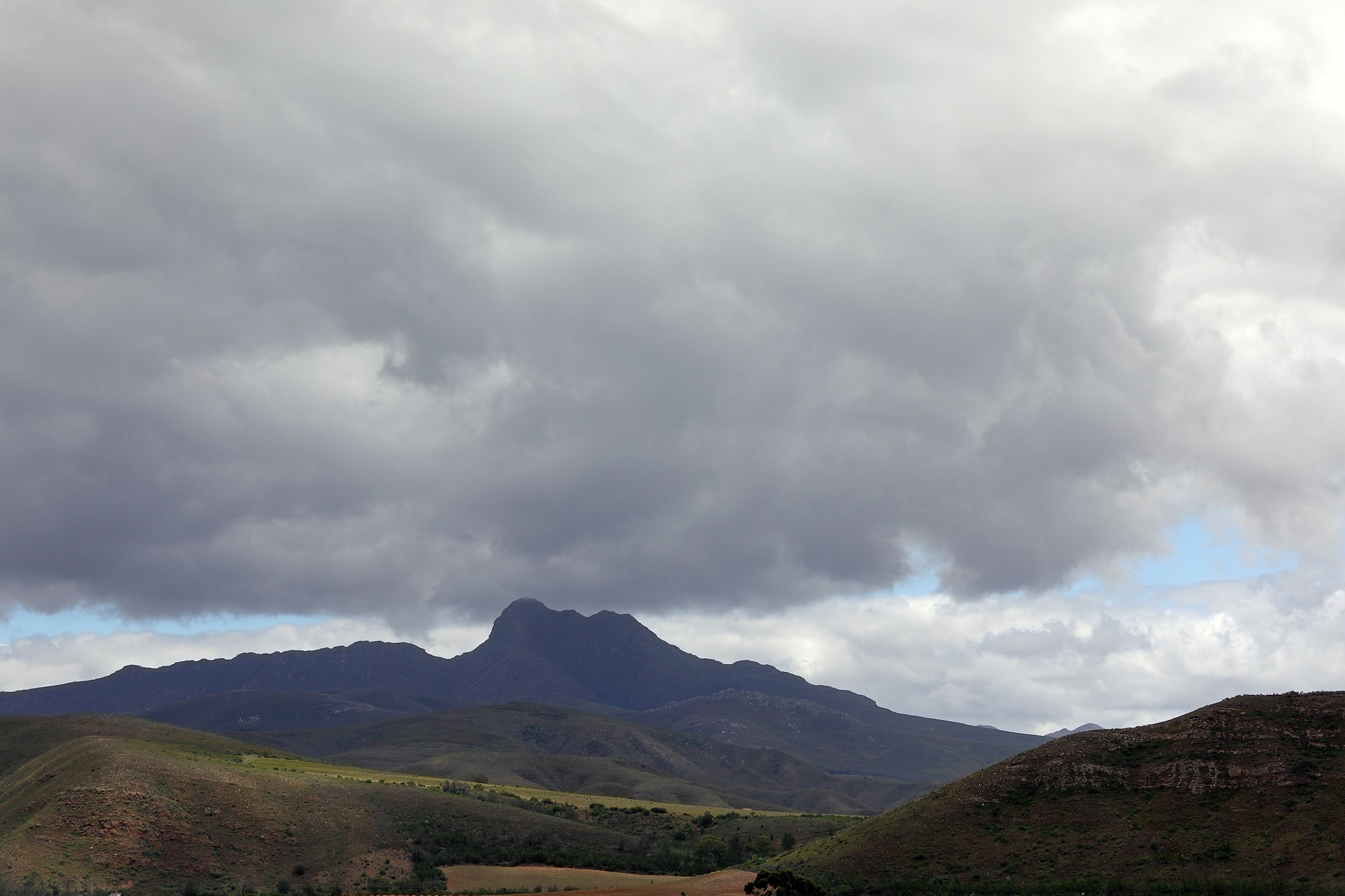 A mountainous landscape with a prominent peak and rolling hills under a cloudy sky.