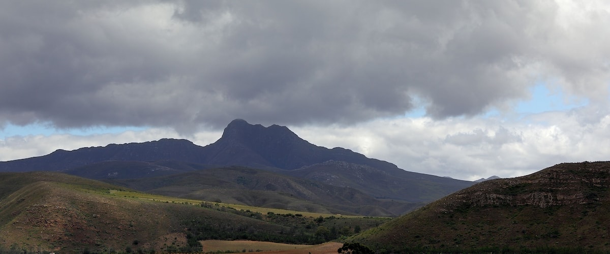 A mountainous landscape with a prominent peak and rolling hills under a cloudy sky.