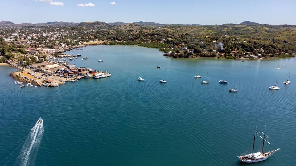 A coastal town with a marina, boats, and a hilly landscape in the background.