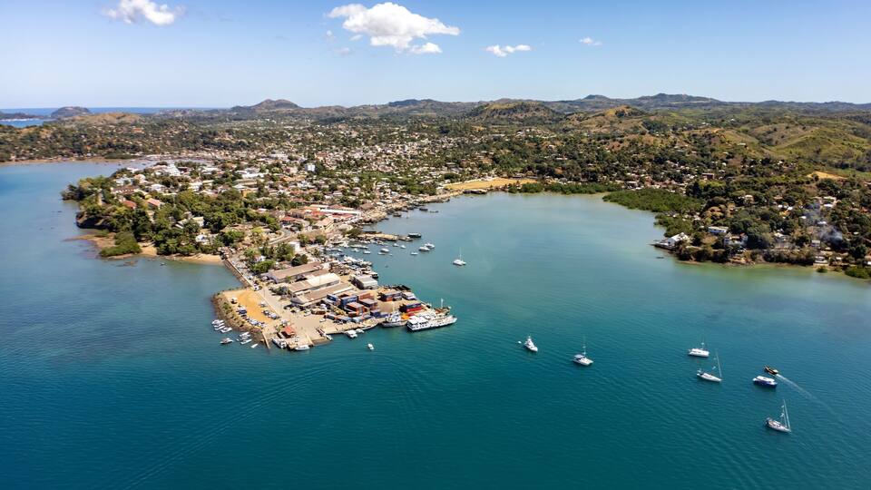 An aerial view of a coastal town with a marina, boats, and surrounding hills.
