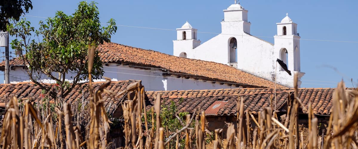 A white church with a cross on top, surrounded by dry vegetation and a clear blue sky.