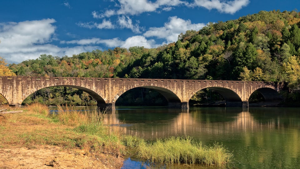 A stone bridge over a river with autumn foliage in the background.
