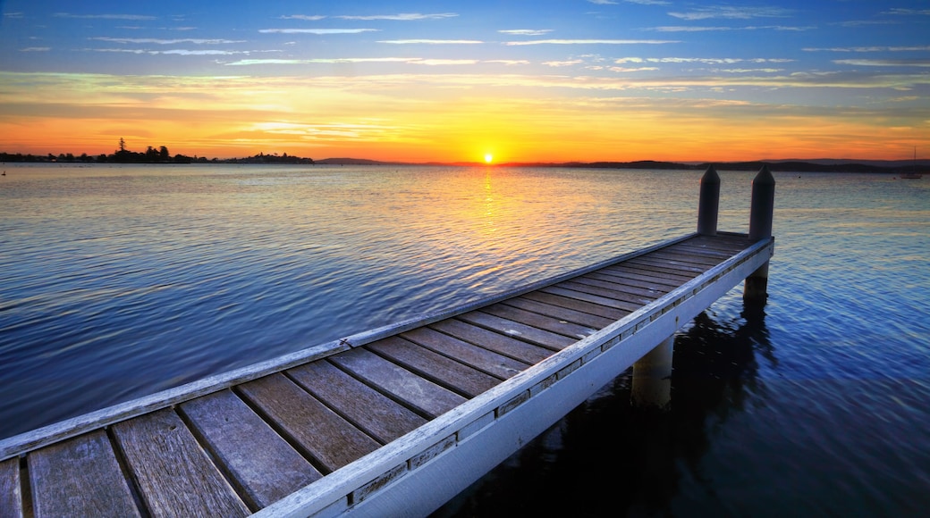Un muelle de madera que se adentra en aguas tranquilas durante el atardecer, con un cielo despejado.