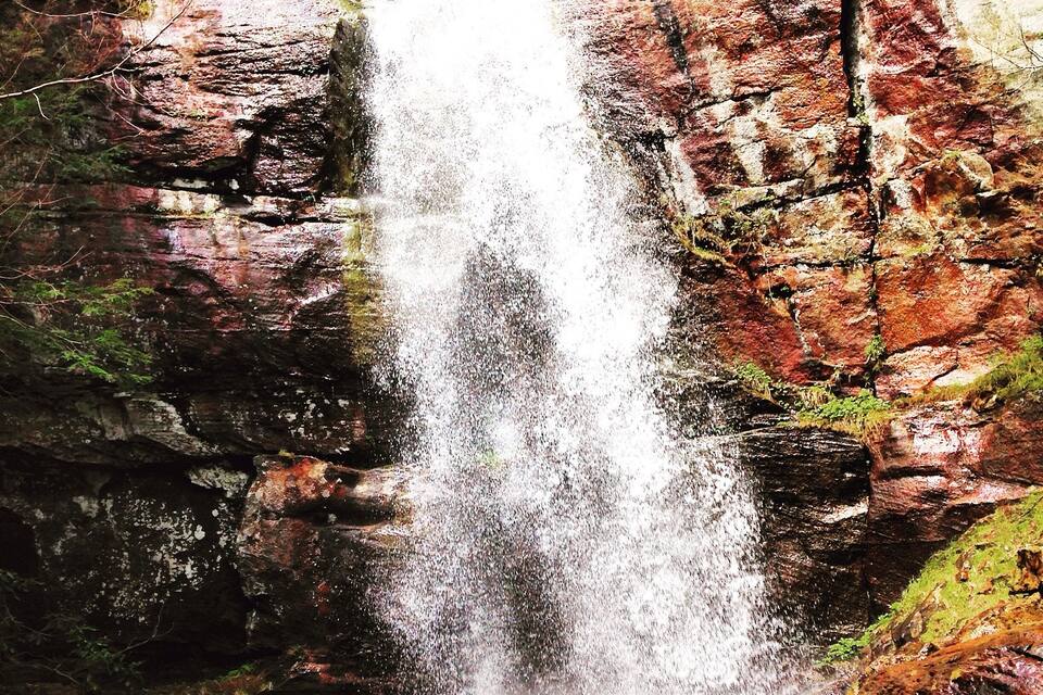 Een waterval die over rotsachtig terrein stroomt, begroeid met mos en begroeiing.