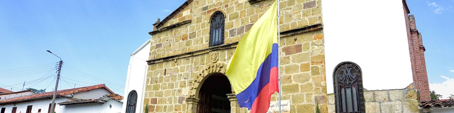 Um edifício de pedra histórico com uma bandeira, plantas em vasos e um céu azul límpido.