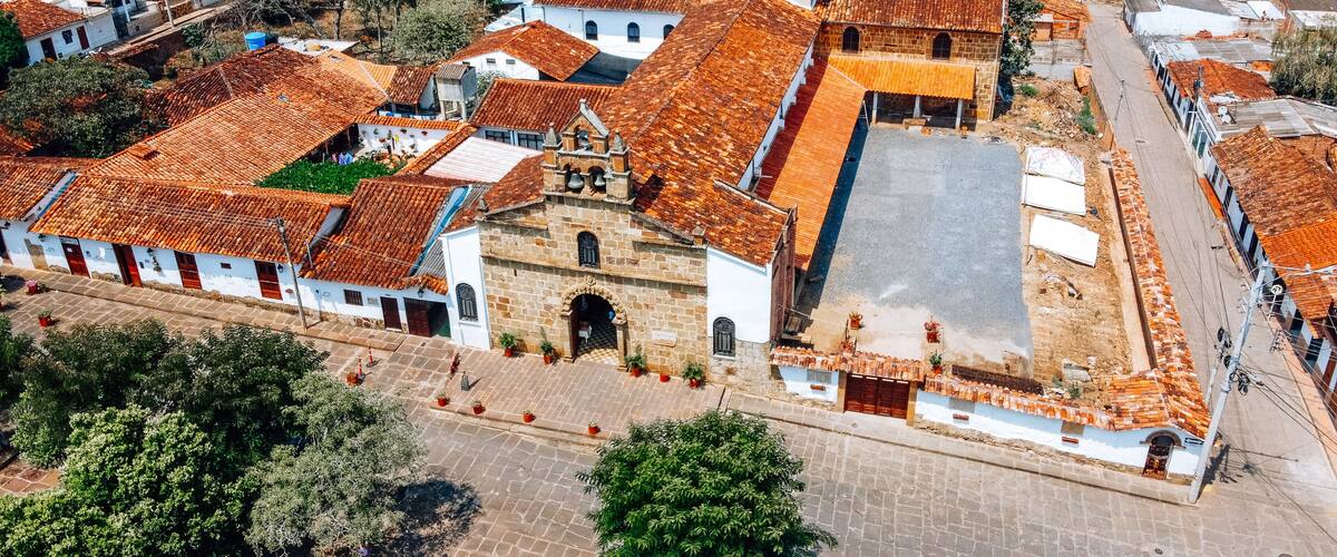 An aerial view of a historic town with terracotta-roofed buildings, a central church, and cobblestone streets.