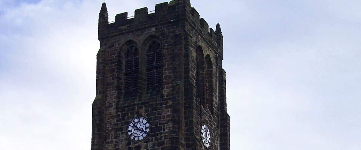 A tall stone church with two clocks and a pointed tower.
