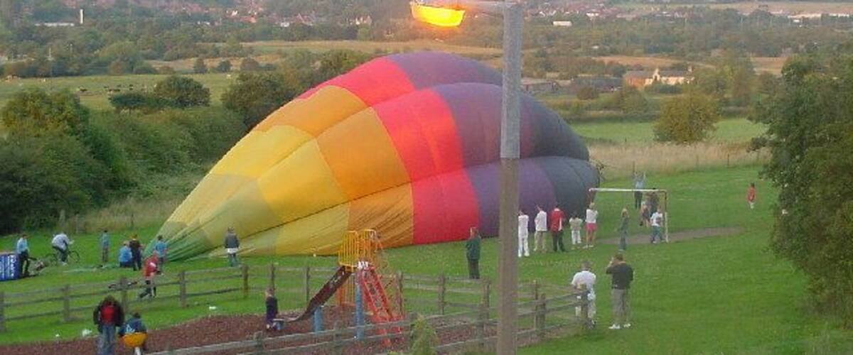 A colorful hot air balloon in a grassy field with a few people and a playground in the background.