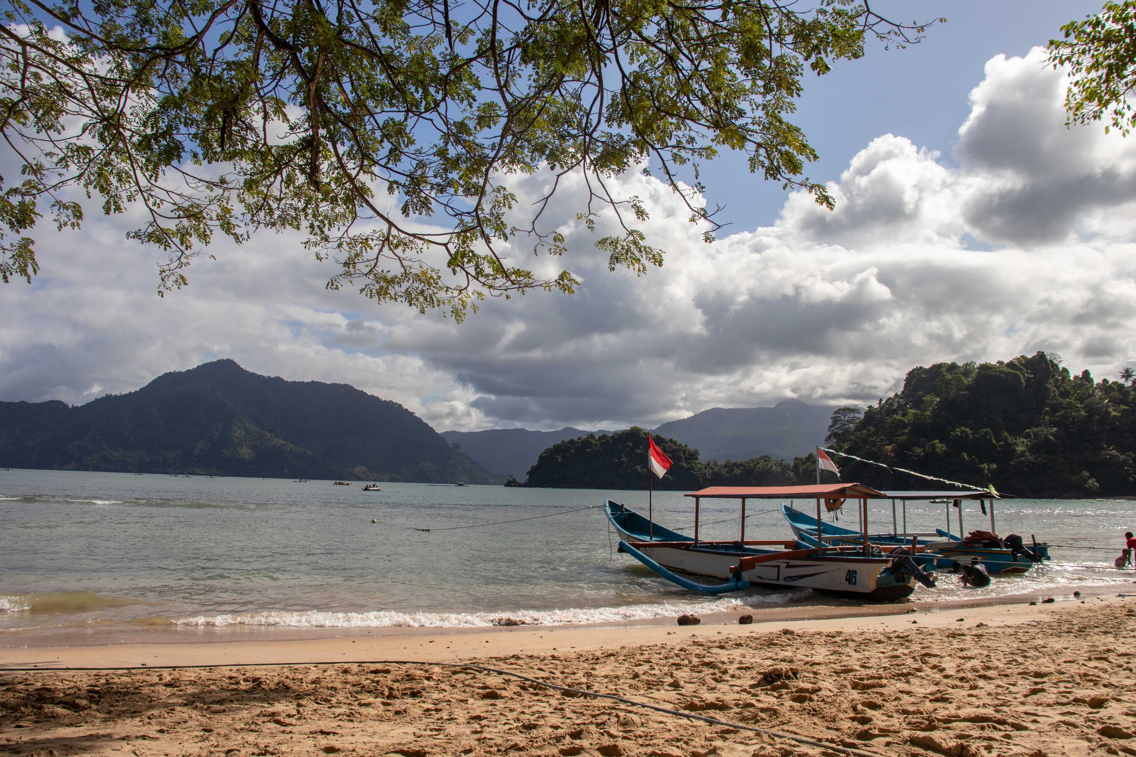 A beach with boats, a flag, and mountains in the background.
