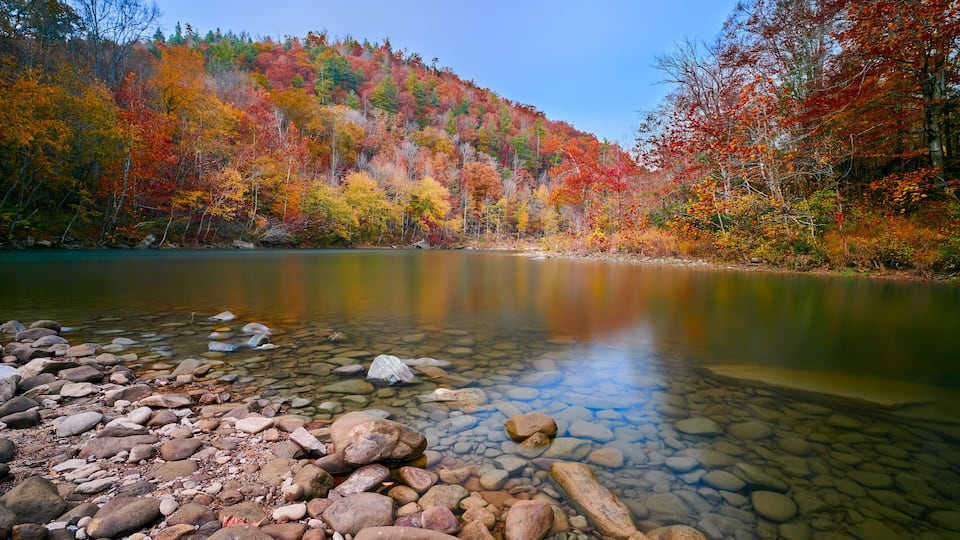 A clear lake surrounded by autumn-colored trees and a rocky shoreline.