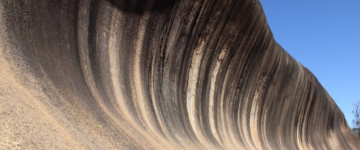 A large, smooth, wave-like rock formation under a clear blue sky.