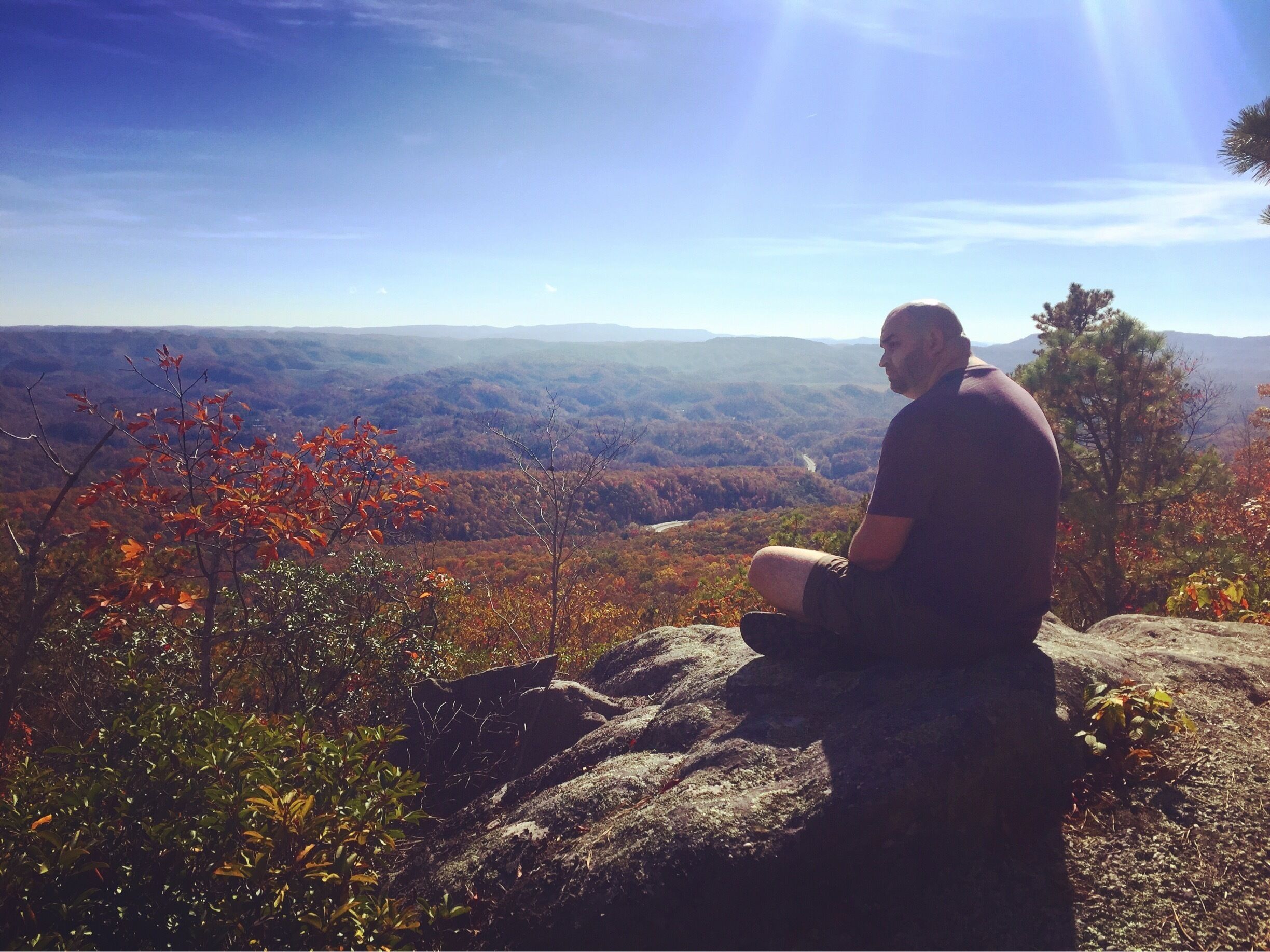 A person sitting on a rock overlooking a mountainous landscape with autumn foliage.
