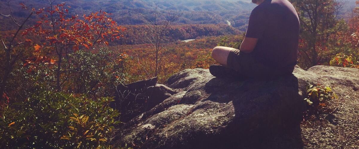 A person sitting on a rock overlooking a mountainous landscape with autumn foliage.