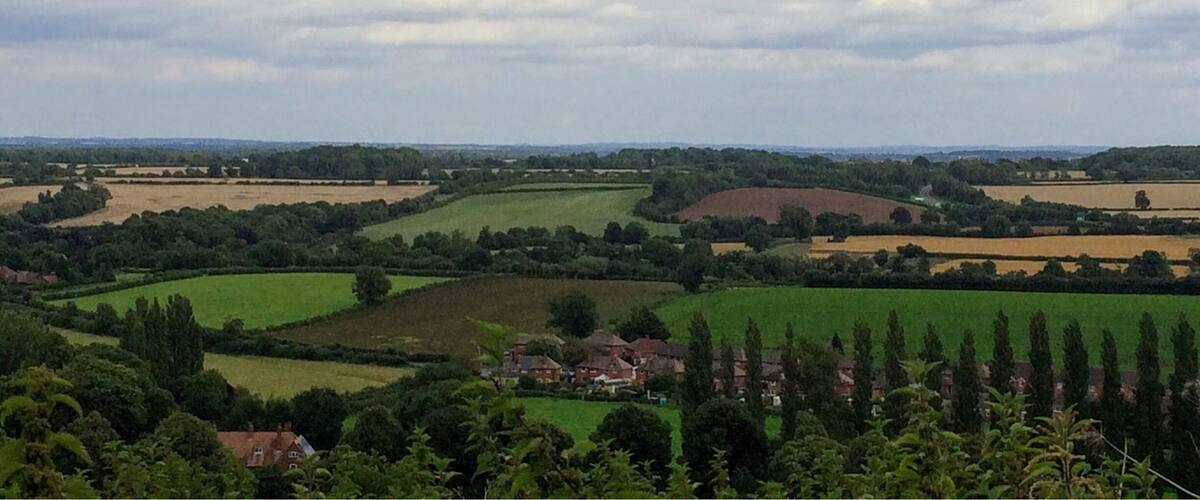 A rural landscape with rolling hills, fields, and scattered houses.