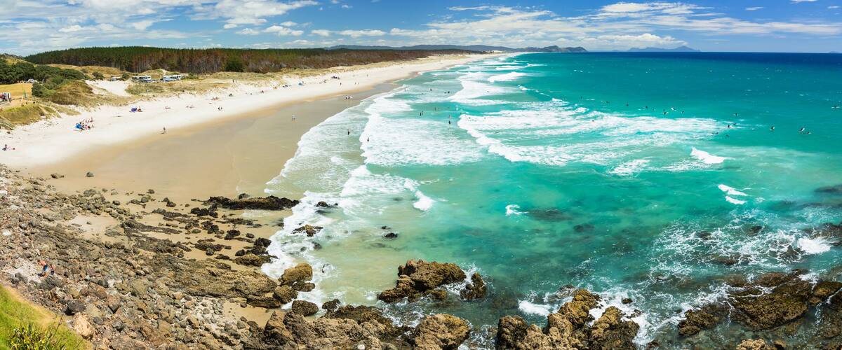 A coastal beach with clear turquoise waters, sandy shore, and rocky outcrops.