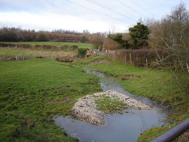 A rural landscape with a small stream, grassy fields, and a fence.