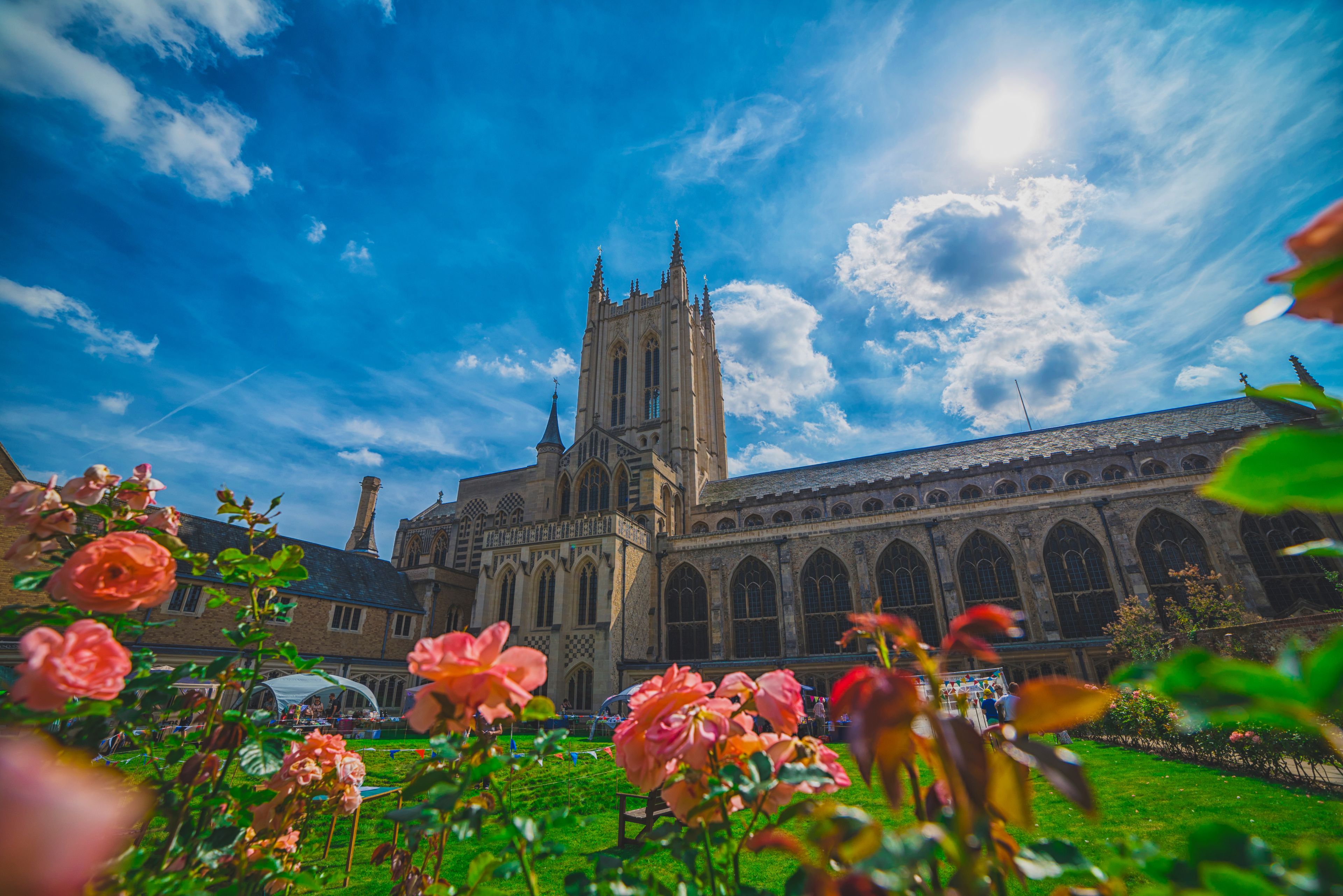 A historic cathedral with a tall spire, surrounded by lush greenery and blooming flowers.
