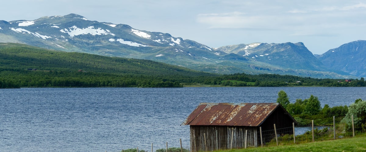 A lake with mountains in the background and a small wooden structure in the foreground.