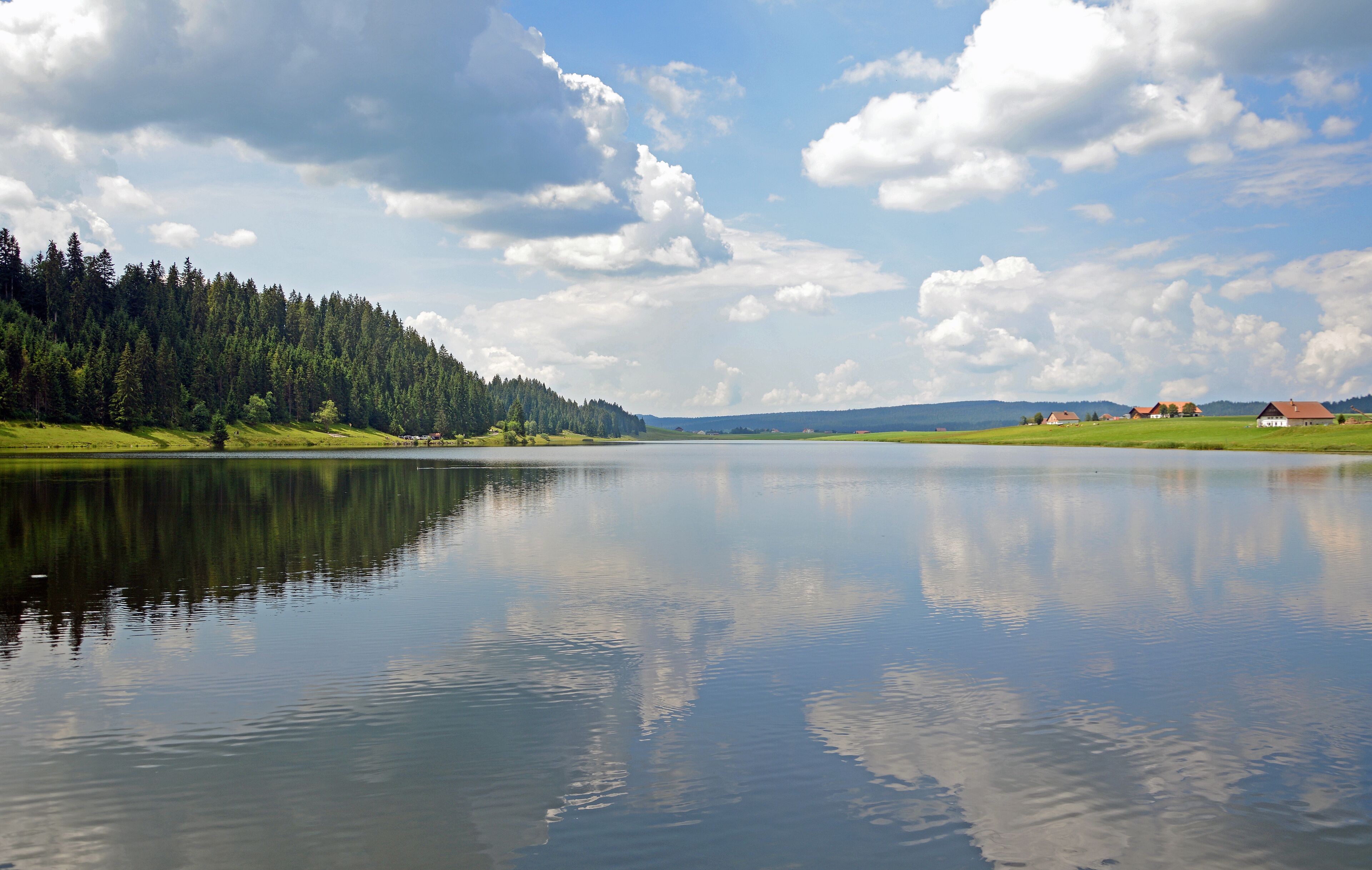 A calm lake with a forested hillside and a few houses in the distance.