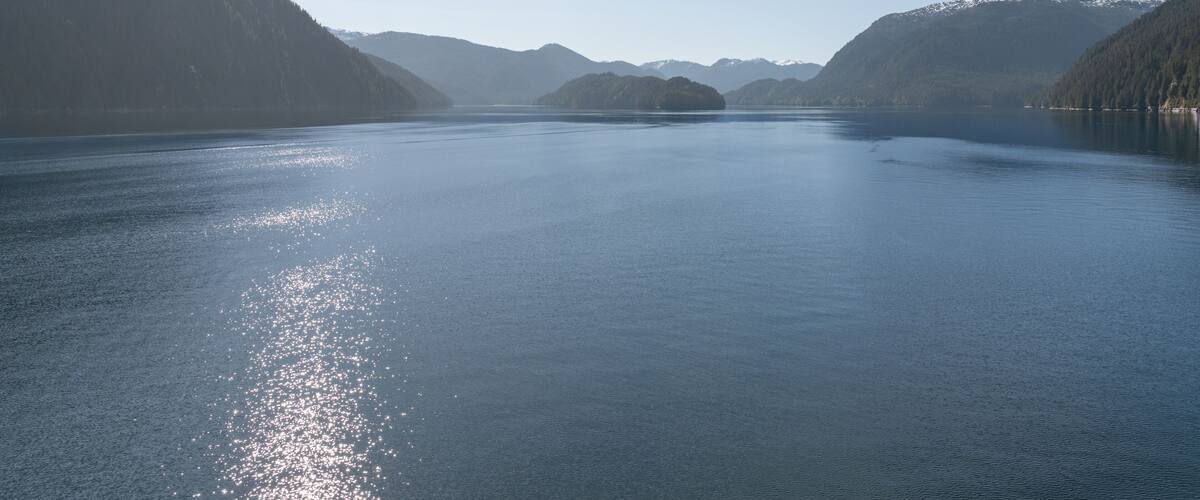 A calm lake surrounded by forested hills under a clear sky.