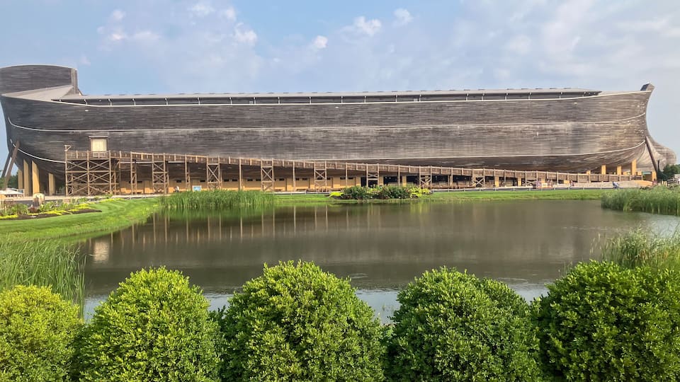 A large ship-shaped building with a surrounding pond and green hedges.
