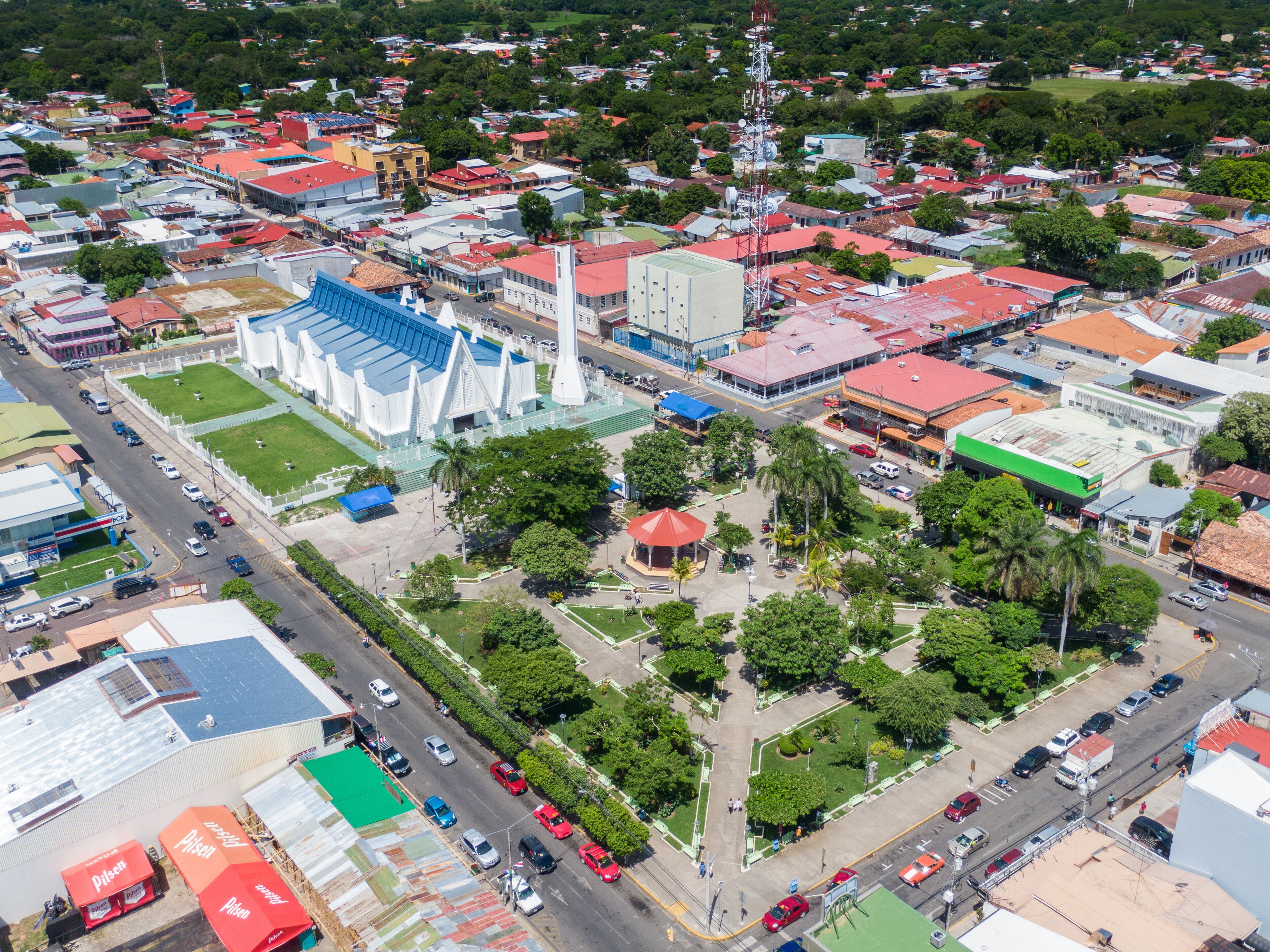 An aerial view of a city with a prominent white church, a large blue sports stadium, and various buildings with red roofs.