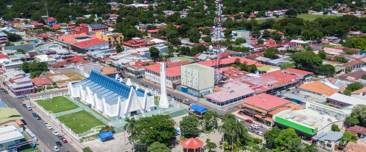 An aerial view of a city with a prominent white church, a large blue sports stadium, and various buildings with red roofs.