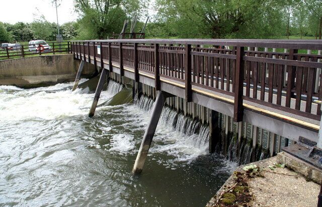 A bridge over a flowing river with a railing and concrete pillars.