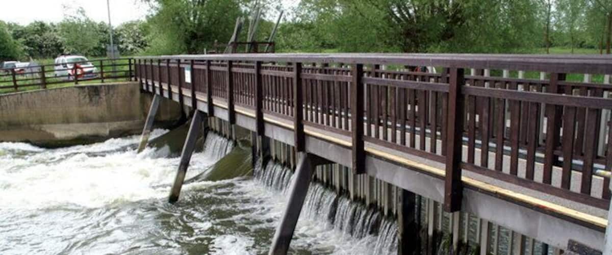 A bridge over a flowing river with a railing and concrete pillars.