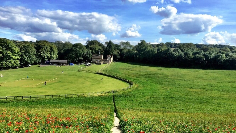 Eine grüne Wiese mit einem Zaun, einem Gebäude und Bäumen im Hintergrund.