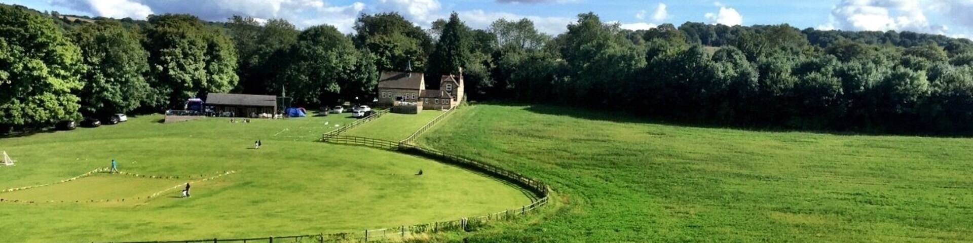 Un campo verde con una valla, un edificio y árboles al fondo.