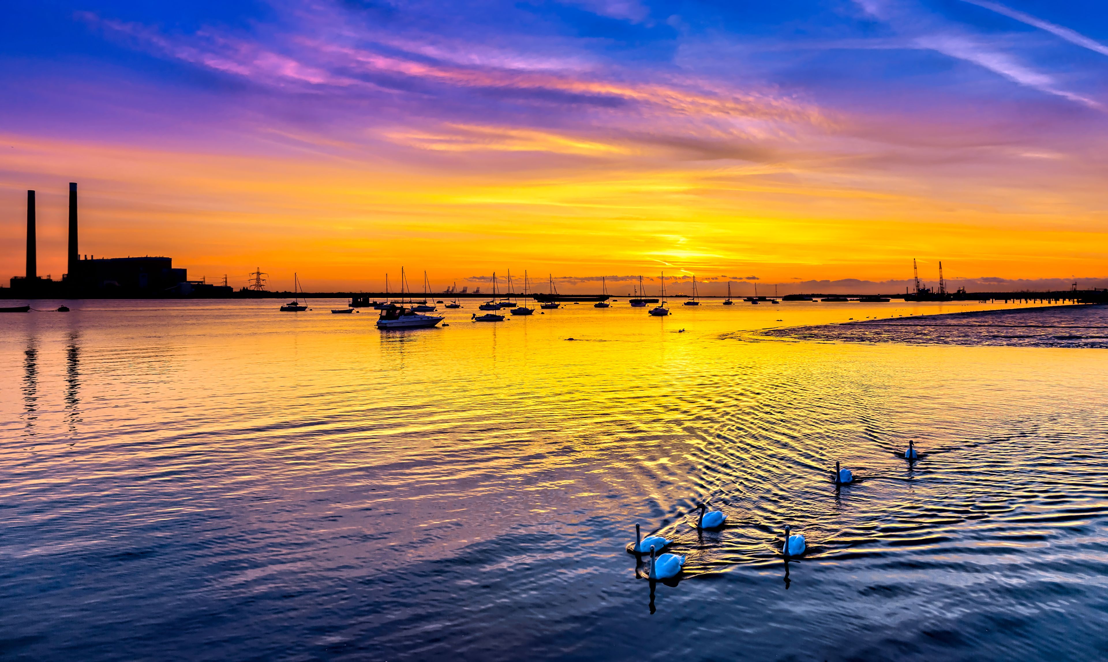A sunset over a calm body of water with boats and a distant industrial structure.
